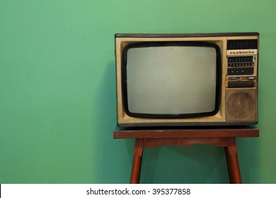 Retro television on old wooden deck with vintage green background.