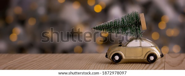 Retro toy\
car carrying tiny Christmas tree against the background of the\
Christmas tree with new year bokeh. Christmas cards.\
Trucking.Delivery service.Copy space for\
text