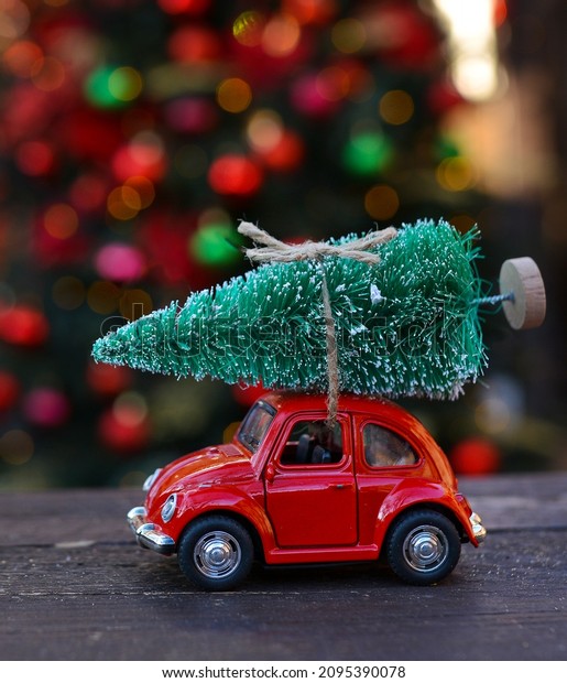 Retro toy red car carrying tiny Christmas tree on\
the background of christmas bokeh. Christmas cards.\
Trucking.Delivery service
