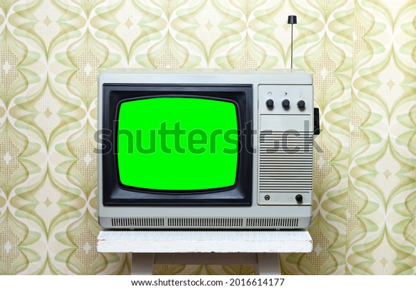 A retro TV with a green screen for adding videos and\
images stands on a chair in a room against a background of vintage\
wallpaper. 