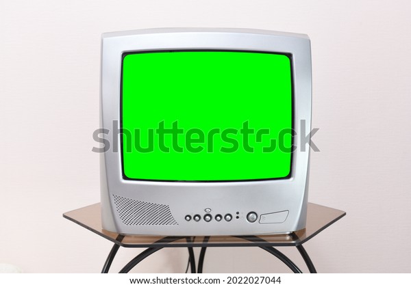 A retro TV with a green screen for adding videos and\
images stands on a table in the room against a background of\
vintage wallpaper. 