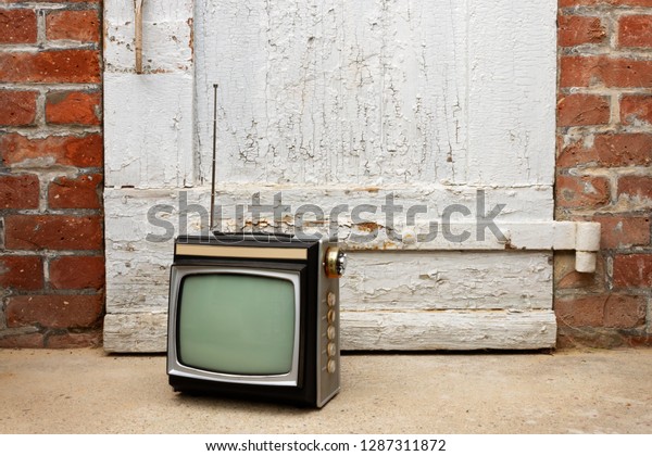 Retro TV as obsolete dusty TV receiver laid\
on stairs in front of old door\
outside