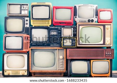 Retro TV receivers set from circa 60s, 70s and 80s of XX century, old wooden television stand with amplifier front mint blue wall background. Broadcasting, news concept. Vintage style filtered photo