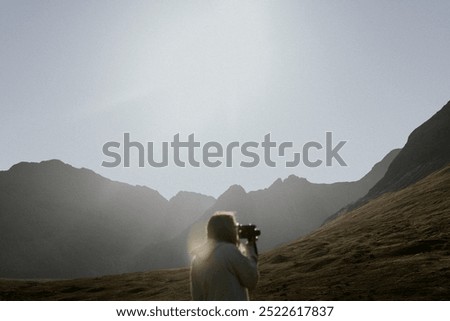 Retro video camera, traveler in Scottish nature. A traveler holding retro video camera taking video of Scottish nature. A traveler with retro camera is taking a video of a Scottish nature landscape.