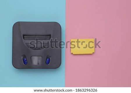 Retro video game console, cartridge on blue pink background. Top view