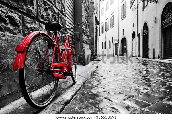 Retro vintage red bike on cobblestone street in the old town. Color in black and white. Old charming bicycle concept.