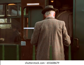 Retro Vintage Styled Photograph Of  Back View  Of Older Man Dressed In A Long Brown Tweed Coat Climbing Into The Carriage Of An Old Steam Train