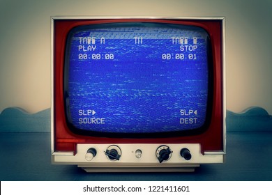 A Retro Vintage TV Showing A VCR Double Deck Tracking An Empty Noisy VHS Tape Screen, Blue Background, Heavy Damage.
