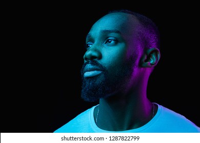 The Retro Wave Or Synth Wave Portrait Of A Young Happy Serious African Man At Studio. High Fashion Male Model In Colorful Bright Neon Lights Posing On Black Background. Art Design Concept
