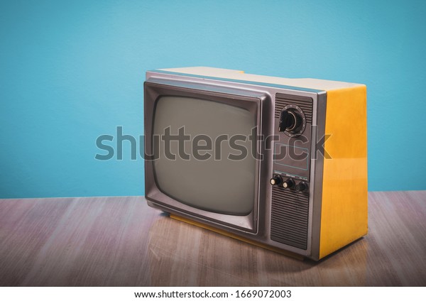 Retro yellow old tv on wooden table with blue concrete\
wall background. 