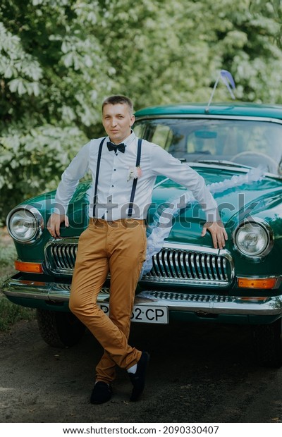 Retro-driver\
in the vintage car on the outdoor background. Handsome groom in the\
car. Confident wealthy young man in suit near classic car. Elegant\
fiance in a suit. Man standing near old\
car.