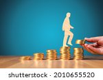 Return on investment, growing savings or wage income concept. Coins and wooden person going on increasing columns of coins. Helping hand adds more money. Successful investment concept.