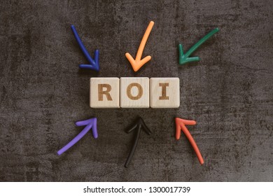 Return On Investment, ROI, Performance Measure Of Business Or Investment Efficiency, Target And Goal, Colorful Arrows Pointing To Cube Wooden Block Building The Word ROI On Chalkboard.