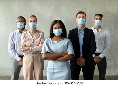 Return To Work Concept. Multiethnic Business Team Wearing Medical Face Masks Posing Together In Office, Diverse Multiracial Coworkers Standing With Folded Arms And Looking At Camera, Free Space