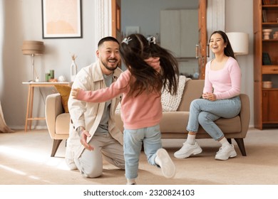 Reunion With Daddy. Asian Kid Daughter Running To Embrace Her Dad, While Mother Sitting On Sofa In Modern Living Room At Home. Family Celebrating Father's Homecoming. Selective Focus - Powered by Shutterstock