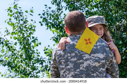 Reunion Of Soldier From New Mexico With Family, Daughter Hug Father. A Girl Holds The Flag Of New Mexico In Her Hand