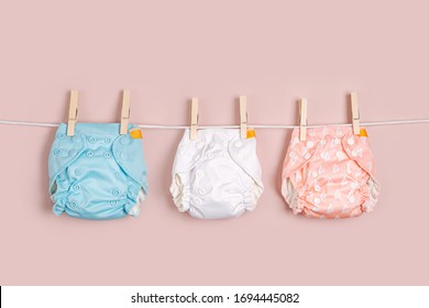 Reusable cloth baby diapers drying on a clothes  line. Eco friendly cloth nappies on a pink background. Sustainable lifestyle. Zero waste concept.