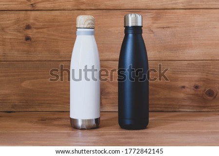 Reusable eco-friendly black and white stainless steel thermo bottles on wooden rustic background. Copy space. Zero waste, no plastic, sustainability. Bring your own water bottle concept.