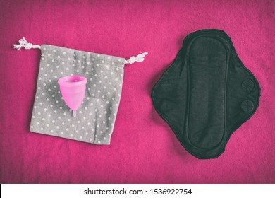 Reusable Eco-friendly Feminine Hygiene Period Products - Menstrual Cup And Black Organic Cotton Menstruation Pad - Cloth Menstrual Pads To Wash. Top View On Red Towel Background.