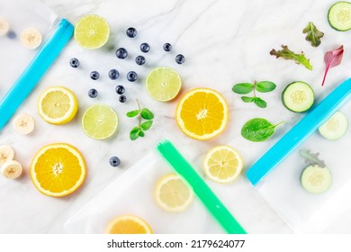 Reusable Food Storage Bags With Fruit And Vegetables, Overhead Flat Lay Shot On A White Marble Kitchen Table. Fresh Summer Produce In Ziplock Containers