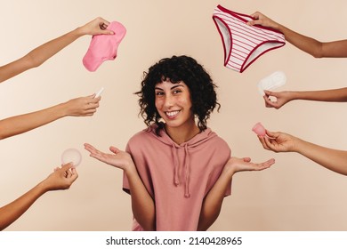 Reusable or non-reusable? Happy young woman smiling at the camera while surrounded by hands holding different sanitary products. Cheerful modern woman making a choice about her feminine hygiene.