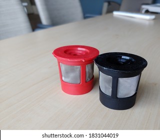 Reusable K Cups For Coffee Machine. Filters Are Red And Black With Fine Mesh. Individual Coffee Pods Are Sitting On A Staff Room Table With Chairs Out Of Focus In The Background. Selective Focus.
