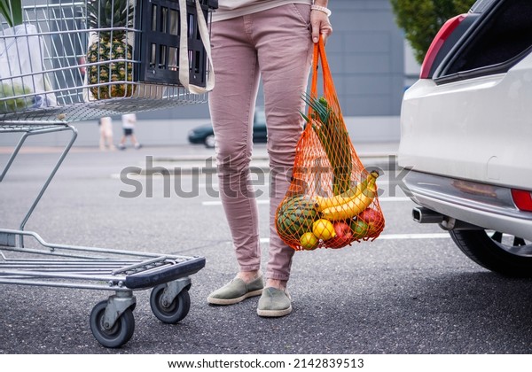 Reusable mesh bag\
with groceries purchased. Woman standing at parking lot after\
plastic free shopping at supermarket. Ethical consumerism and\
sustainable lifestyle with zero\
waste