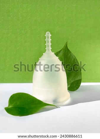 A reusable silicone menstrual cup with green leaf on a green colored paper background, an eco-friendly low impact menstruation product.