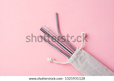 reusable stainless steel straws and cleaning brush in white cotton bag on pink background, eco friendly lifestyle