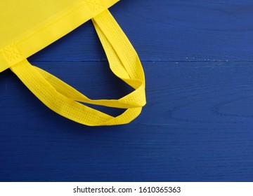 Reusable yellow viscose bag on blue wooden background, plastic waste reduction concept