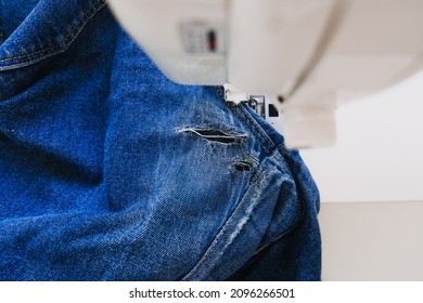 Reuse, Repair, Upcycle. Denim Upcycling Ideas, Repair And Using Old Jeans. Close-up Of Sewing Machine With Shabby, Old, Torn Denim Jeans Fabric. Sewing Studio Working Process.