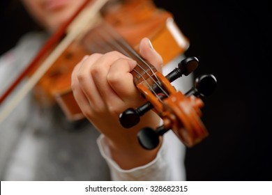 Stell dich in den Klang ein. Nahaufnahme von professioneller Geige in Händen eines kleinen Mädchens, das sie hält und beim Stehen einzeln auf schwarzem Hintergrund spielt
