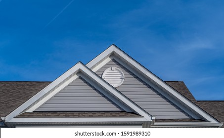 Reverse double gable close up on luxury single family residential home. 
White round louver vent. Roof line of traditional home with one gable running one way and reverse gables running the other.
