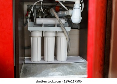 Reverse osmosis water purification system in red closet at home. Installation of water purification filters under kitchen sink in red cupboard. Clear water concept