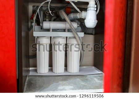 Reverse osmosis water purification system in red closet at home. Installation of water purification filters under kitchen sink in red cupboard. Clear water concept