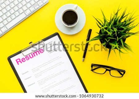 Review resumes of applicants. Resume on yellow work desk with coffee, glasses, keyboard top view