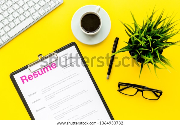 Review resumes of applicants.\
Resume on yellow work desk with coffee, glasses, keyboard top\
view
