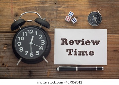 Review Time written on paper with wooden background desk,clock,dice,compass and pen.Top view conceptual