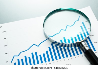 Reviewing Financial Report. Looking At Growth Chart With Magnifying Glass. Document, Chart And Magnifying Glass On Gray Reflection Background.
