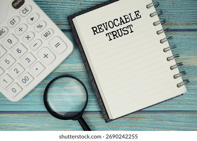 Revocable Trust text on notepad with magnifying glass and calculator on wooden background
