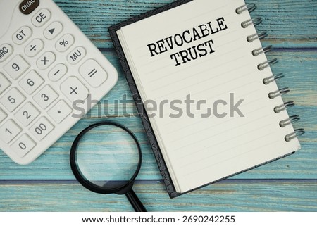 Revocable Trust text on notepad with magnifying glass and calculator on wooden background