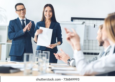 rewarded happy manageress holding blank paper while colleagues clapping to her