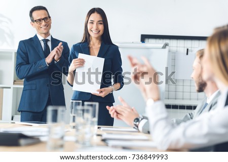 rewarded happy manageress holding blank paper while colleagues clapping to her