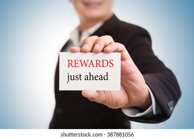 Rewards Just Ahead Message Word On Card In Hand Of Friendly Man Hand And Smiling