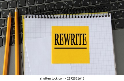 REWRITE - word on a yellow piece of paper on the background of a laptop with a notebook and a pen. Business concept