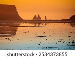 Reynisdrangar, basalt sea stacks in southern Iceland, bathed in the golden hues of sunrise, with the low tide water reflecting the colours on Reynisfjara black sand beach