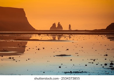 Reynisdrangar, basalt sea stacks in southern Iceland, bathed in the golden hues of sunrise, with the low tide water reflecting the colours on Reynisfjara black sand beach - Powered by Shutterstock