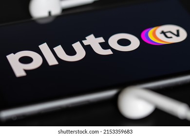 Rheinbach, Germany  28 April 2022,  The brand logo of the streaming service "Pluto TV" on the display of a smartphone with headphones (focus on the brand logo)