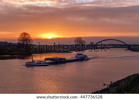 Rhine barge sailing on the river near a bridge at sunset