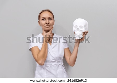 Rhinoplasty and aesthetic medicine. Adult Caucasian pretty woman holds cranium and touches her face. Concept of plastic surgery and professional cosmetology.